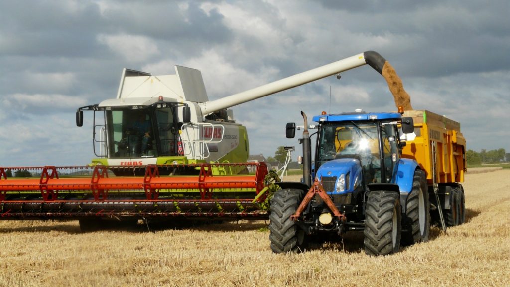 A combine harvester pouring grain into a trailer pulled by a tractor